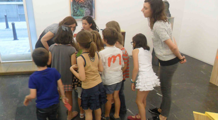 Olga Adelantado, rodeada de niños, ante la atenta mirada de Isabel Puig en el taller para pequeños de la galería Luis Adelantado.